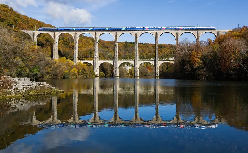 A double-decker TGV crossing a stone viaduct in the French countryside