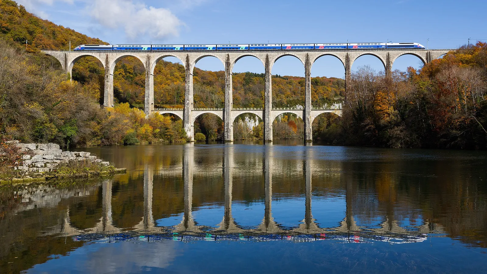 A double-decker TGV crossing a stone viaduct in the French countryside