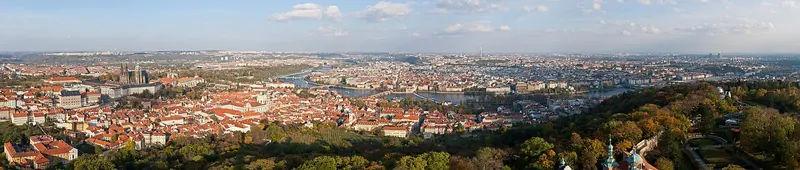A wide panorama of a European city of red roofs, spires and a river at dusk
