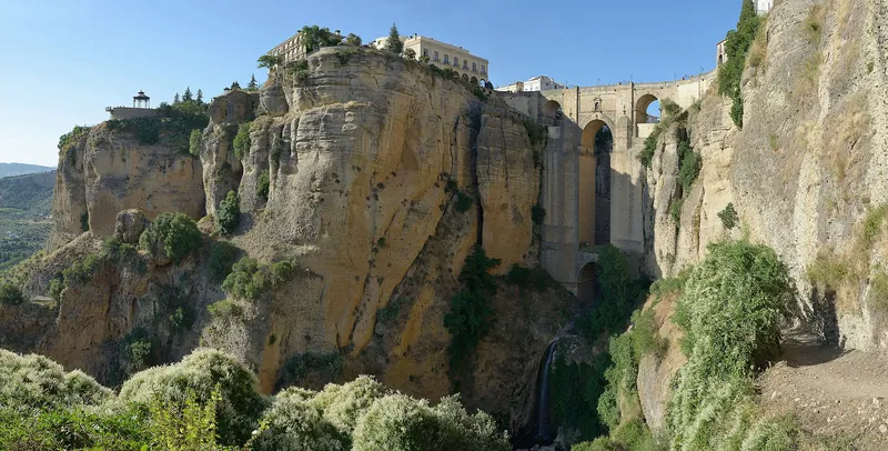 A stone bridge spanning a deep gorge beneath a hilltop town