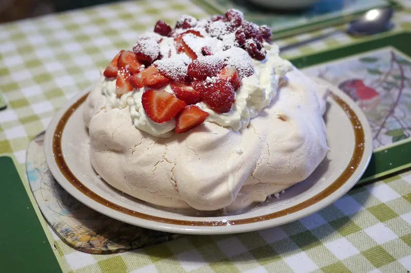 A pavlova meringue dessert topped with cream and strawberries
