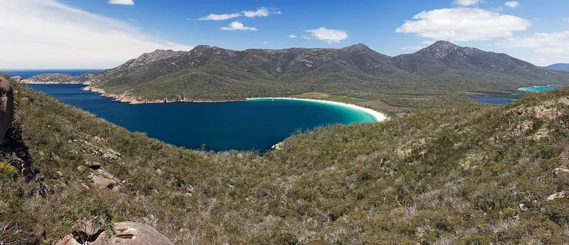 The white crescent of Wineglass Bay between forested granite peaks in Tasmania