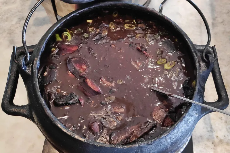 A pot of feijoada, black bean stew with pork, served with rice and collard greens