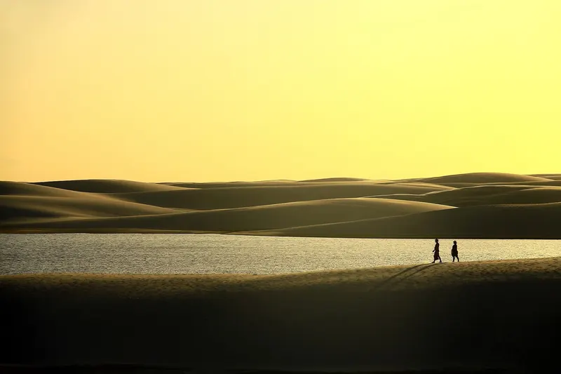 Two tourists walking on a dune at sunset in Lençóis Maranhenses