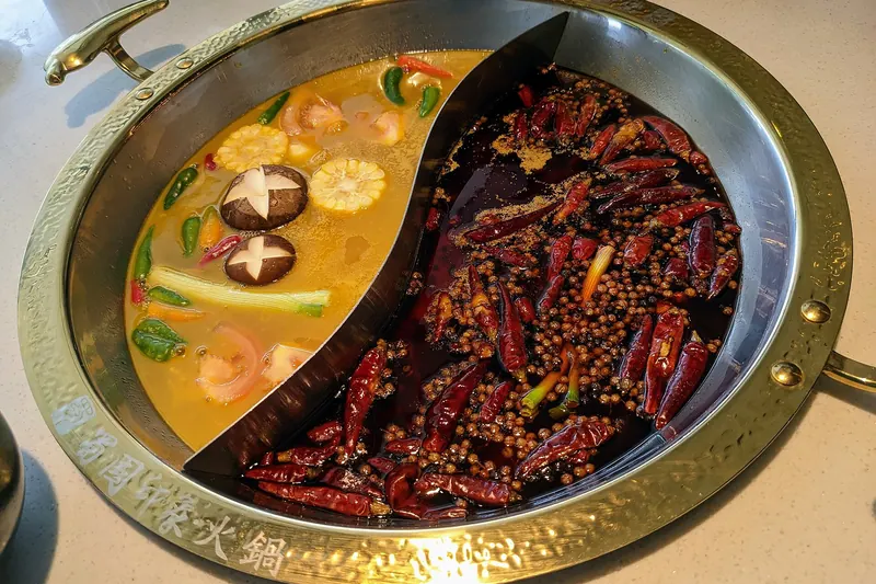 A divided hotpot with red spicy broth on one side, bubbling on a table burner
