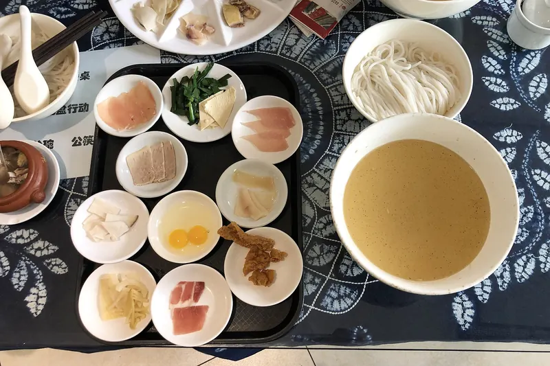 Crossing-the-bridge noodles served with raw ingredients around a bowl of scalding broth