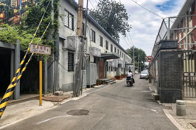 A quiet Beijing hutong lane lined with grey-brick courtyard walls