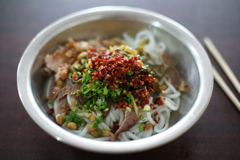 A bowl of Guilin rice noodles topped with peanuts and pickled vegetables