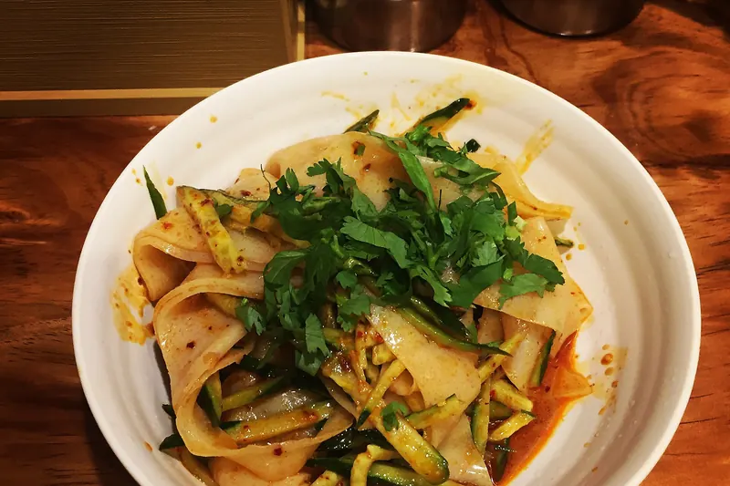 A bowl of cold liangpi noodles tossed with chilli oil and vegetables