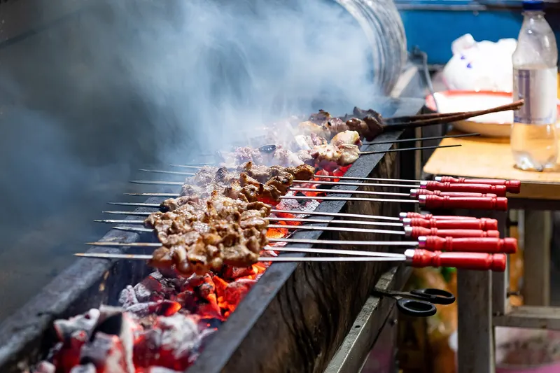 Cumin-dusted lamb skewers cooking over a charcoal grill