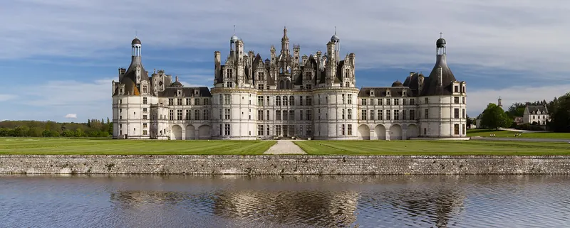 The turreted roofline and long facade of the Château de Chambord reflected in water