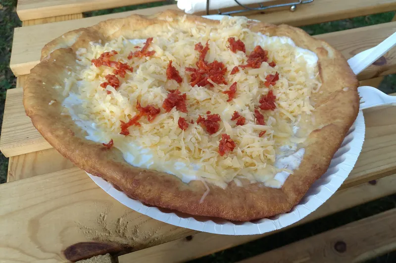 A deep-fried lángos topped with sour cream and cheese