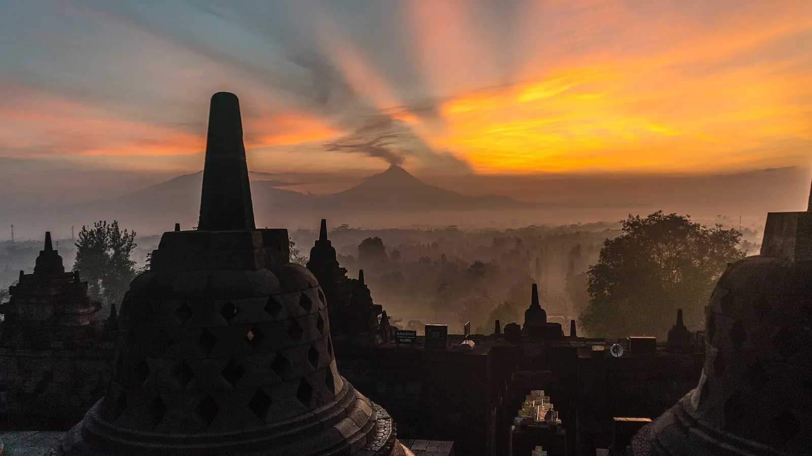 Sunrise over Borobudur temple with a volcano visible in the background