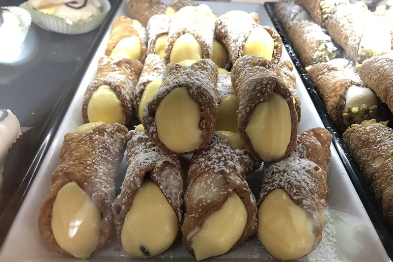 Cannoli filled with sweetened ricotta, their pastry shells dusted with sugar