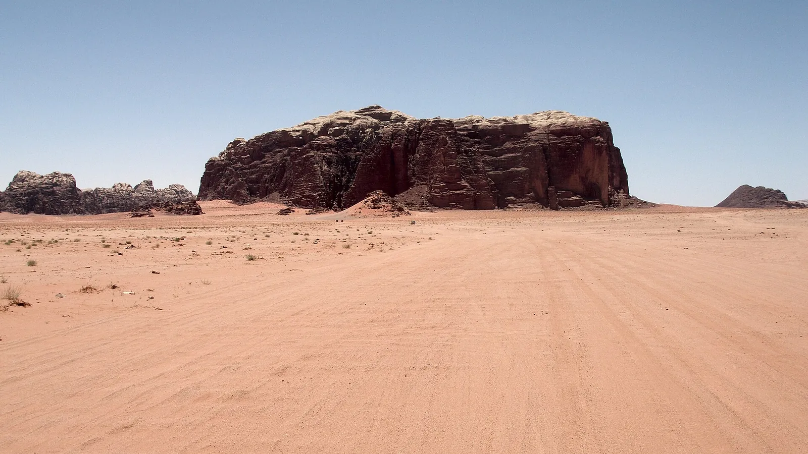 Sandstone hills rising from the red desert floor of Wadi Rum under a wide sky