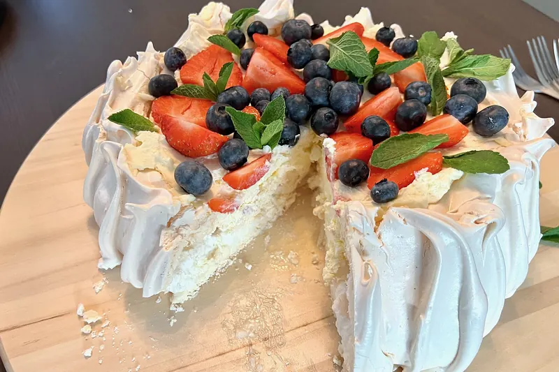 A pavlova dessert topped with cream and fresh fruit