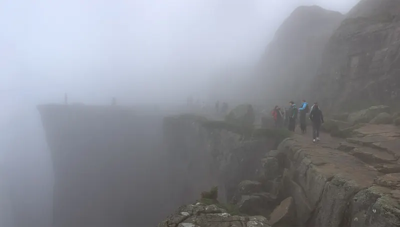 Hikers approaching the edge of Preikestolen through morning fog