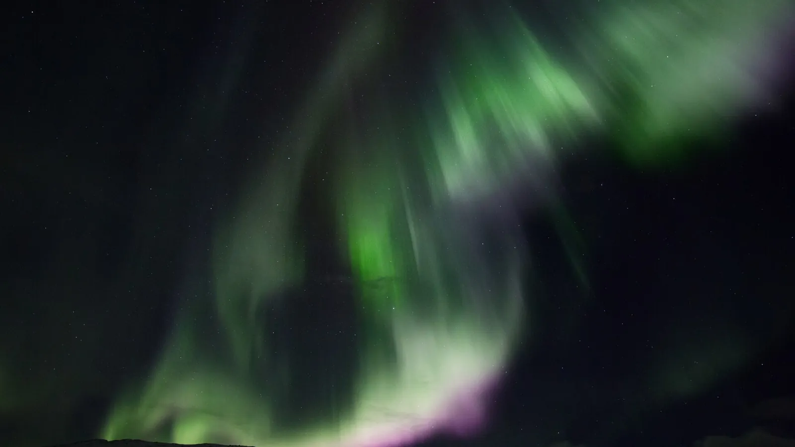 The aurora borealis glowing green over the Arctic landscape near Tromsø