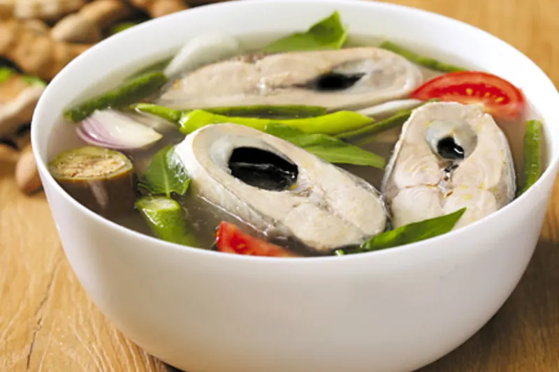 A bowl of sour sinigang soup with fish and vegetables