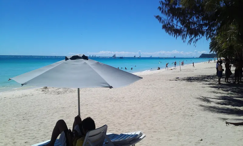 The wide white sand of White Beach on Boracay with palms and blue water