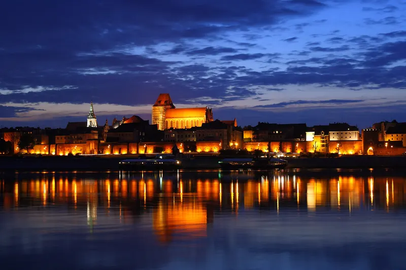 The old town skyline of Toruń lit up at night beside the Vistula