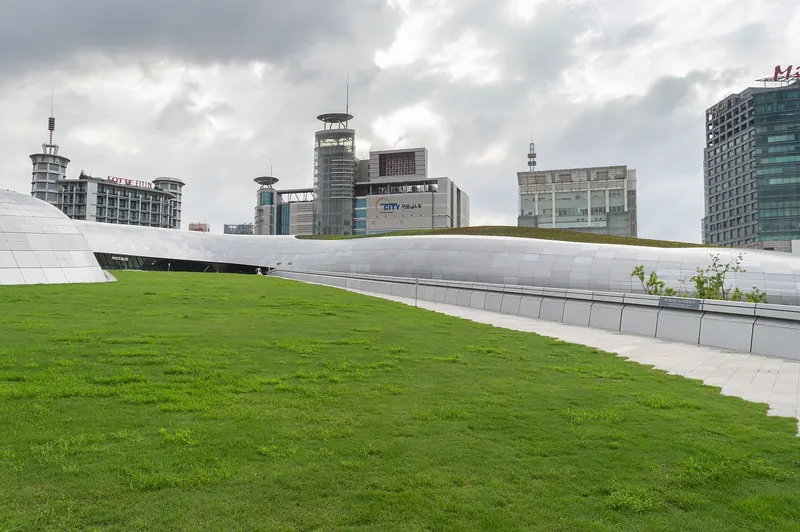 The curved silver walls of Dongdaemun Design Plaza above a garden of grass