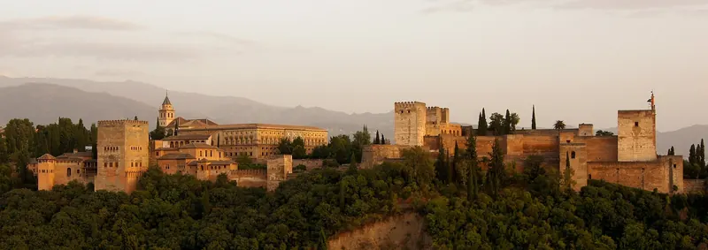The Alhambra palace complex on its ridge with the Sierra Nevada behind at dusk