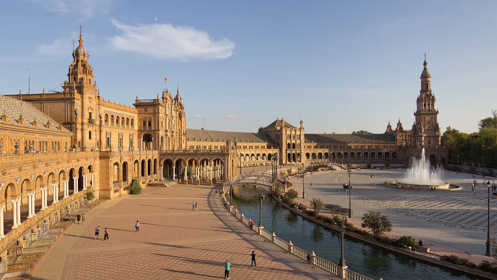 The curved brick and tile facade of the Plaza de España in Seville reflected in its canal