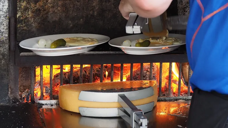 Melted raclette cheese being scraped over potatoes
