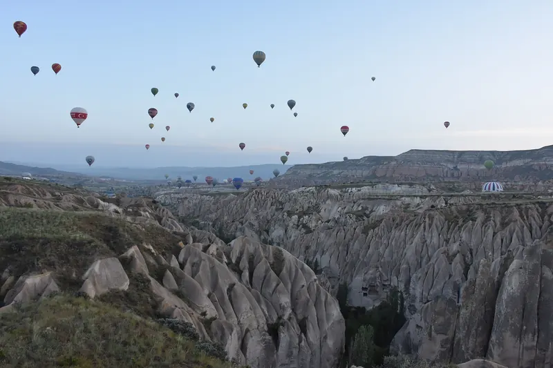 Dozens of hot-air balloons rising over the eroded rock valleys of Cappadocia at dawn