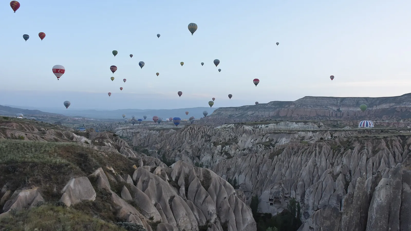 Dozens of hot-air balloons rising over the eroded rock valleys of Cappadocia at dawn