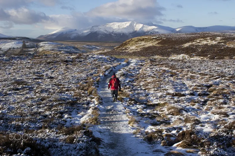 A hiker walking a path across snow-dusted fellside