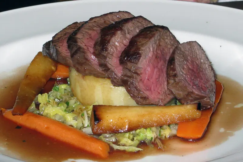 Sliced venison loin plated with roasted vegetables and gravy