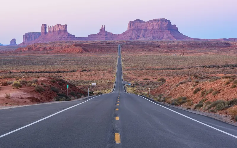 A straight desert road running towards the sandstone buttes of Monument Valley