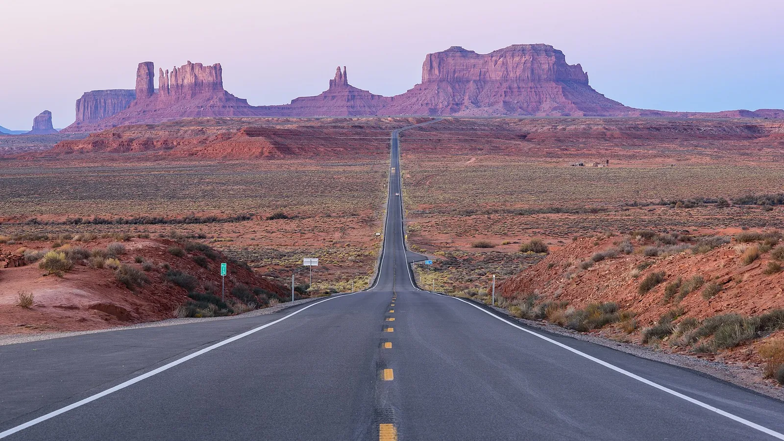 A straight desert road running towards the sandstone buttes of Monument Valley